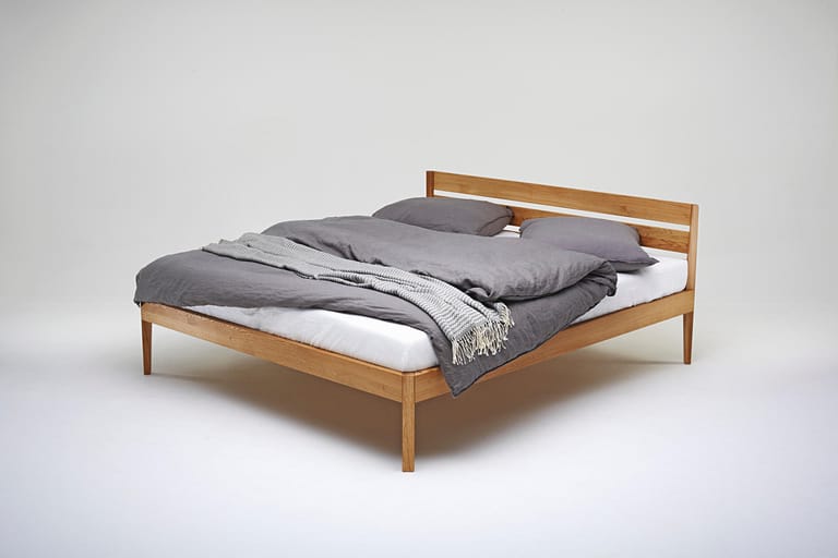 Bleibt der sichtbare Boden unter dem Bett frei, wirkt auch ein kleines Schlafzimmer mit solch einem filigranen Massivholzbett luftig.