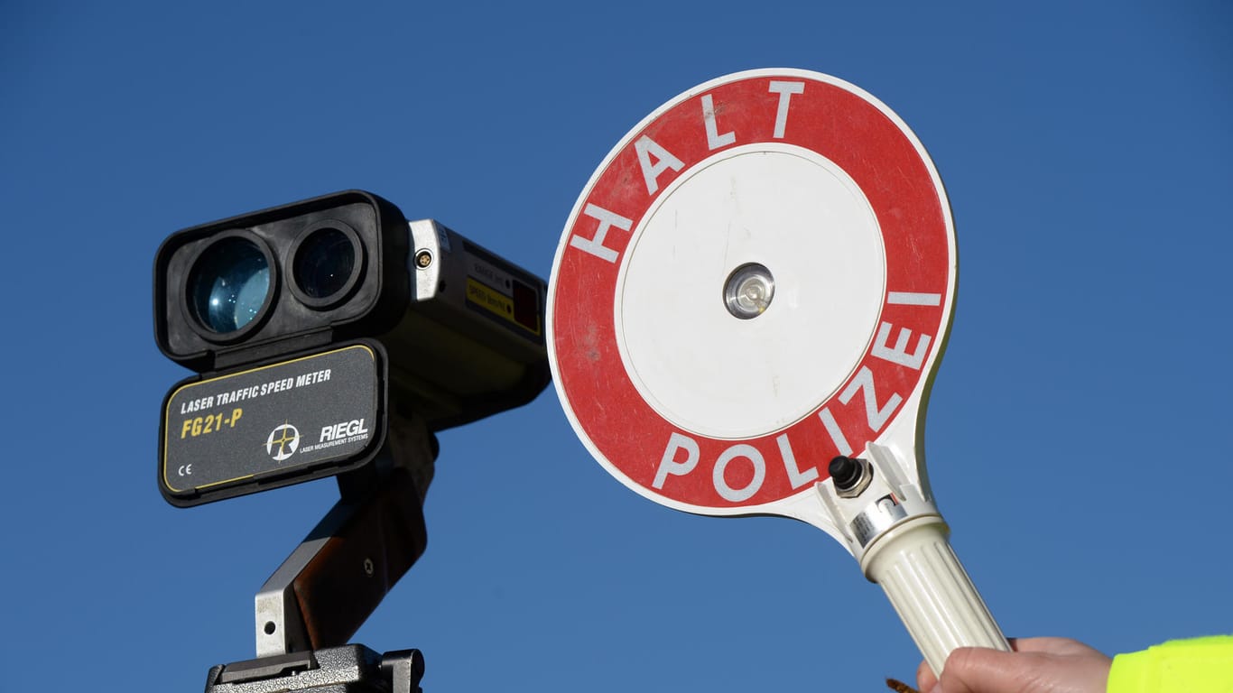 Ein Polizist hält eine Anhaltekelle neben einem Geschwindigkeitsmessgerät hoch.