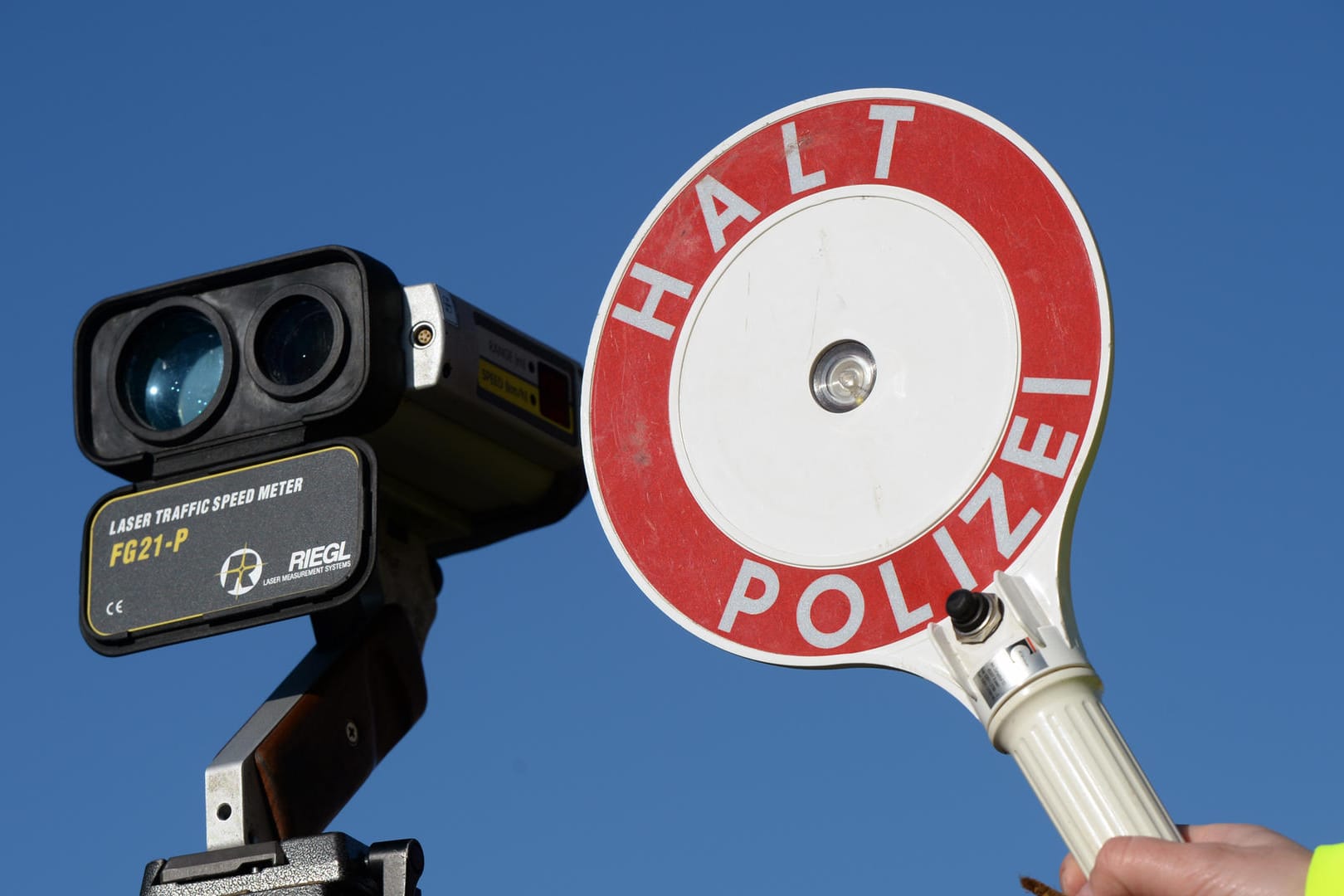 Ein Polizist hält eine Anhaltekelle neben einem Geschwindigkeitsmessgerät hoch.