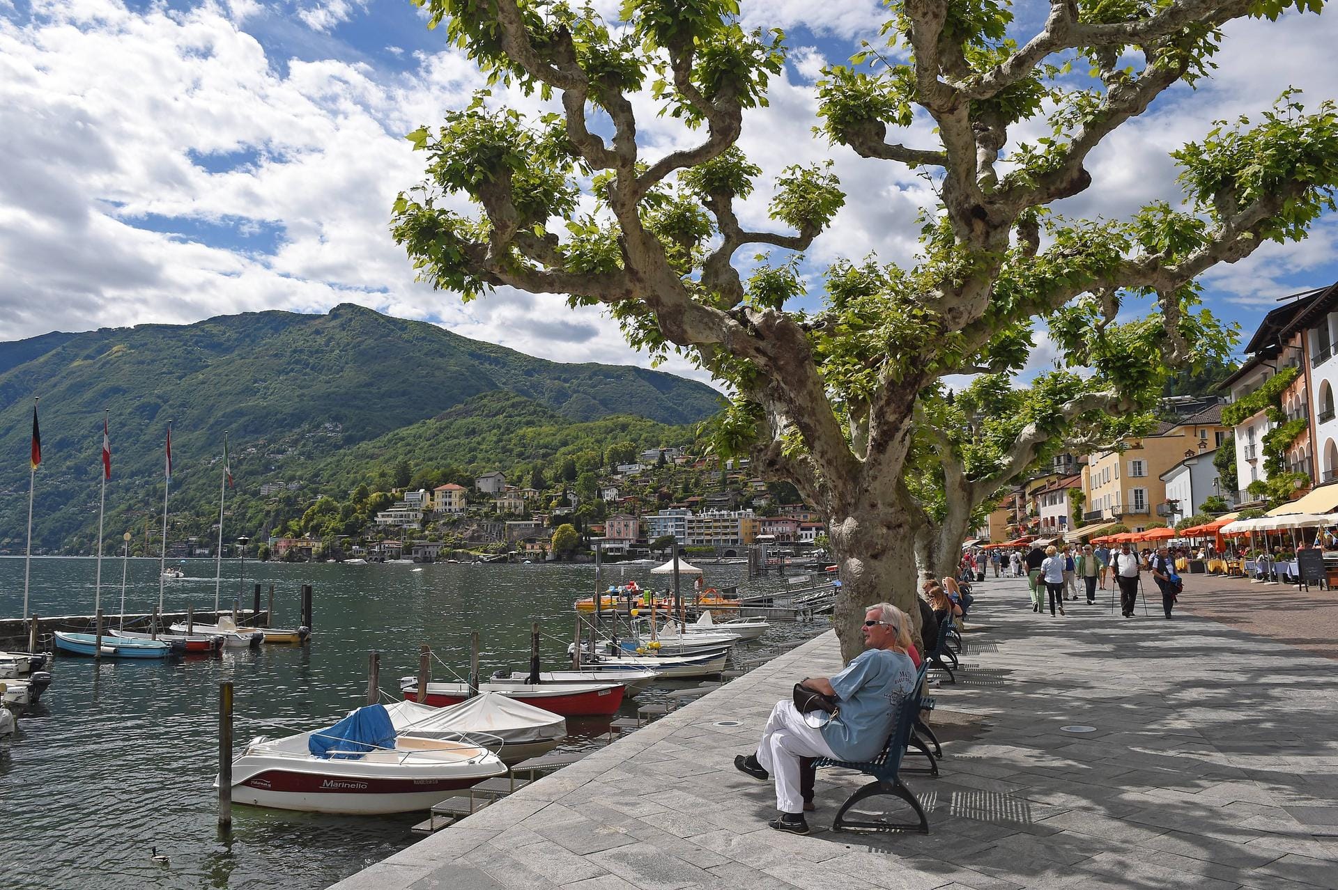 Spaziergang entlang der Seepromenade von Ascona. Menschen genießen das schöne sonnige Wetter am See.