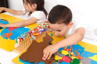 Kinder einer Montessori-Schule arbeiten selbständig mit Geografie-Material. In Montessori-Schulen werden Zeugnisse häufig als individueller Text formuliert.
