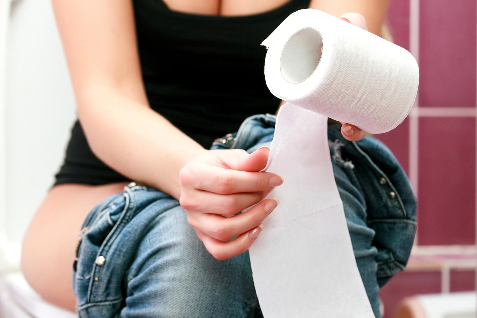 Frau sitzt auf der Toilette mit Klopapier in der Hand.