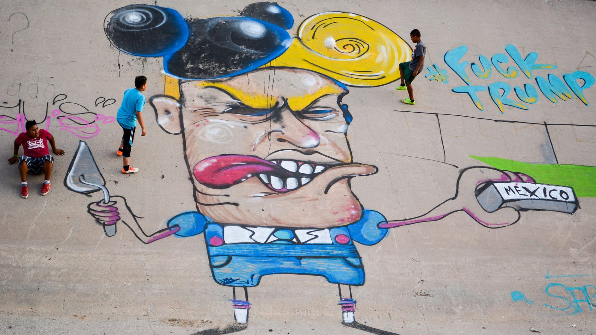 Kinder spielen im Flussbett des Rio Grande neben einer Graffiti-Karikatur des republikanischen US-Präsidentschaftsanwärters Donald Trump. Kinder spielen im Flussbett des Rio Grande neben einer Graffiti-Karikatur des republikanischen US-Präsidentschaftsanwärters Donald Trump.