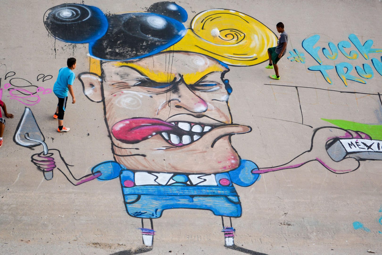 Kinder spielen im Flussbett des Rio Grande neben einer Graffiti-Karikatur des republikanischen US-Präsidentschaftsanwärters Donald Trump.