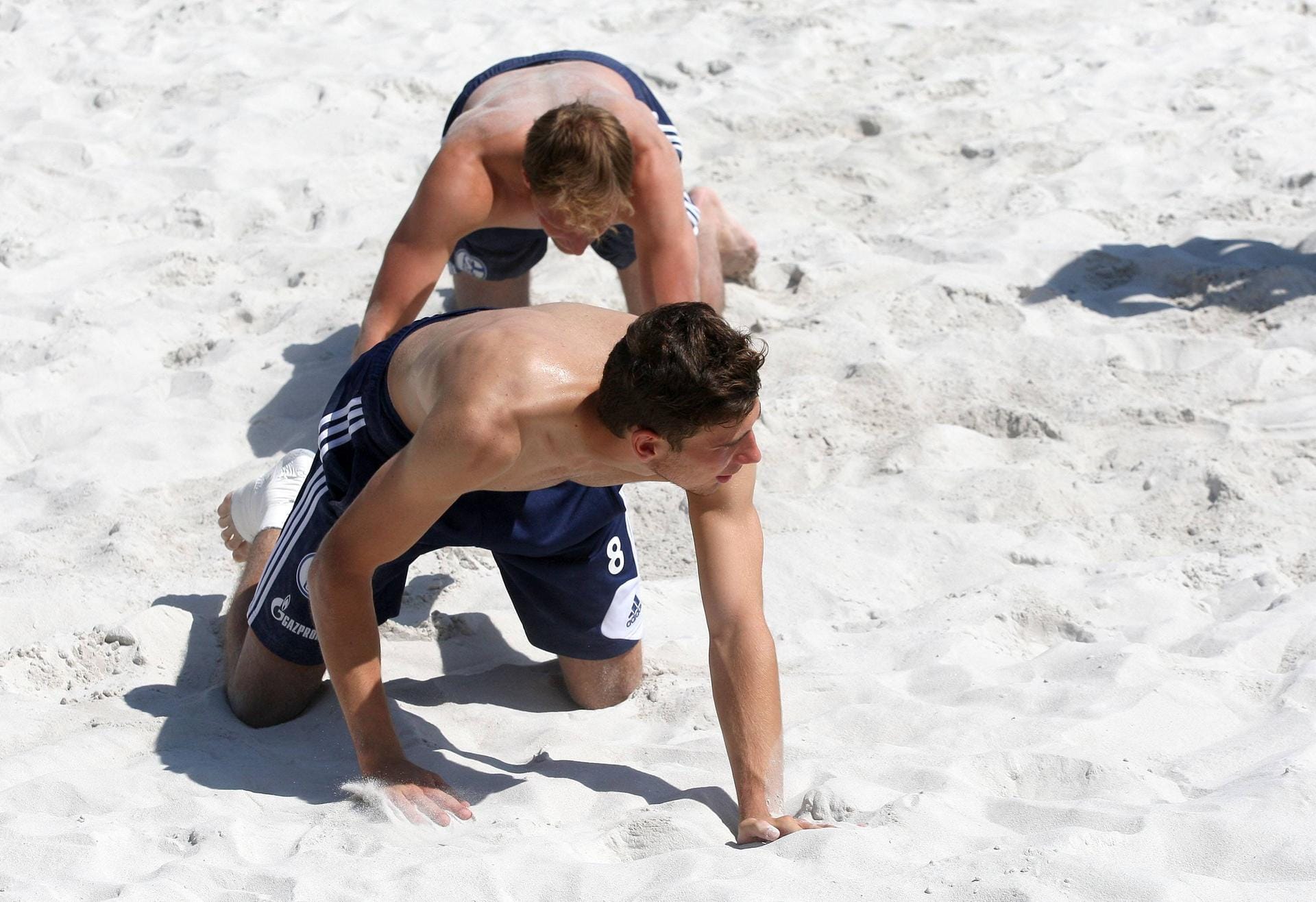 Leon Goretzka und Benedikt Höwedes krabbeln durch den Sand. Die offiziell mitgelieferte Bildbeschreibung nennt das, offenbar ironisch, "Beachvolleyball".