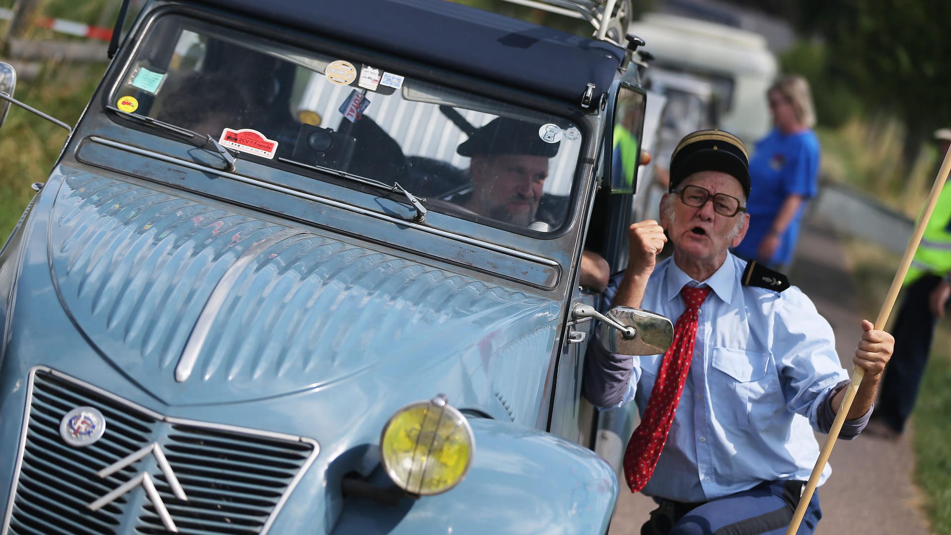 Ein als Gendarm verkleideter Schauspieler begrüßt am 27.07.2016 in Mechernich den Fahrer eines Citroën 2CV.