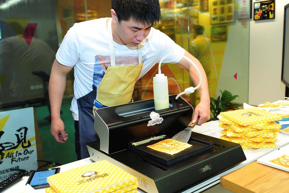 Ein Mann druckt auf einem 3D-Drucker Eierpfannkuchen aus.