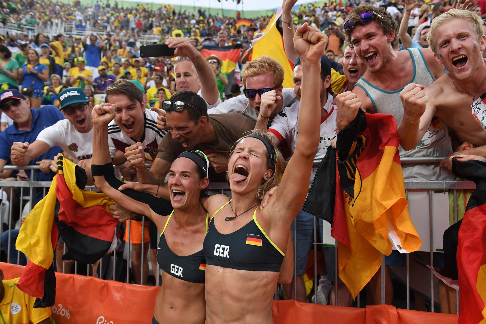 An der Copacabana jubelt Schwarz-Rot-Gold! Die Beachvolleyballerinnen Kira Walkenhorst (li.) und Laura Ludwig (re.) feiern mit deutschen Fans ihren Einzug ins olympische Finale. Die Weltranglistenersten besiegten in ihrem Halbfinale die Brasilianerinnen Larissa/Talita in 2:0- Sätzen mit 21:18, 21:12 und dürfen weiter von der Goldmedaille träumen.