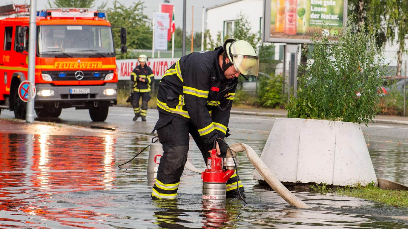 Feuerwehrleute pumpen in Hamburg-Wilhelmsburg Wasser von einem Parkplatz.
