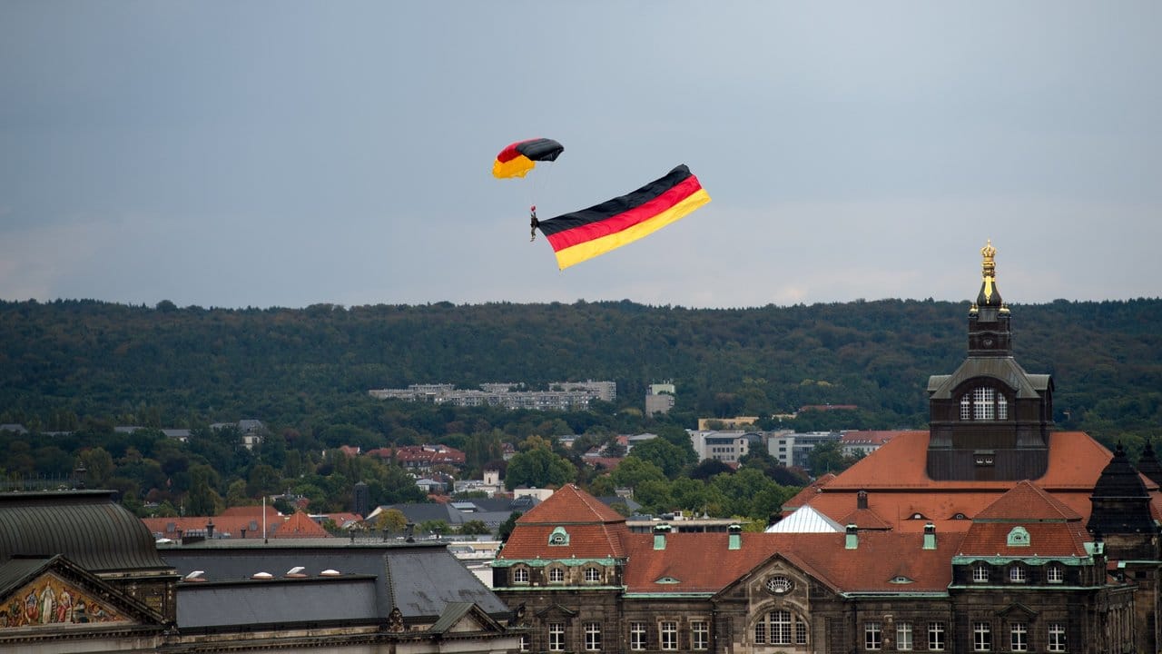 Ein Fallschirmspringer über Dresden zieht eine Deutschlandfahne hinter sich her. Ein Fallschirmspringer über Dresden zieht eine Deutschlandfahne hinter sich her.