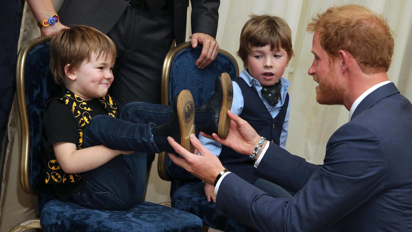 Prinz Harry bewundert die Batman-Schuhsohlen eines kleinen Gastes im Dorchester Hotel.