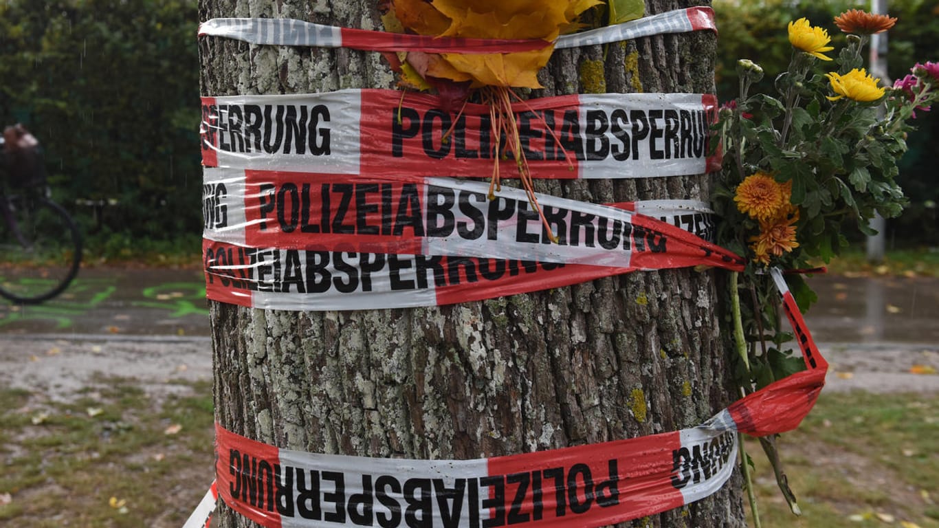 Blumen sind mit einem Absperrband der Polizei an einem Baum in Freiburg befestigt.