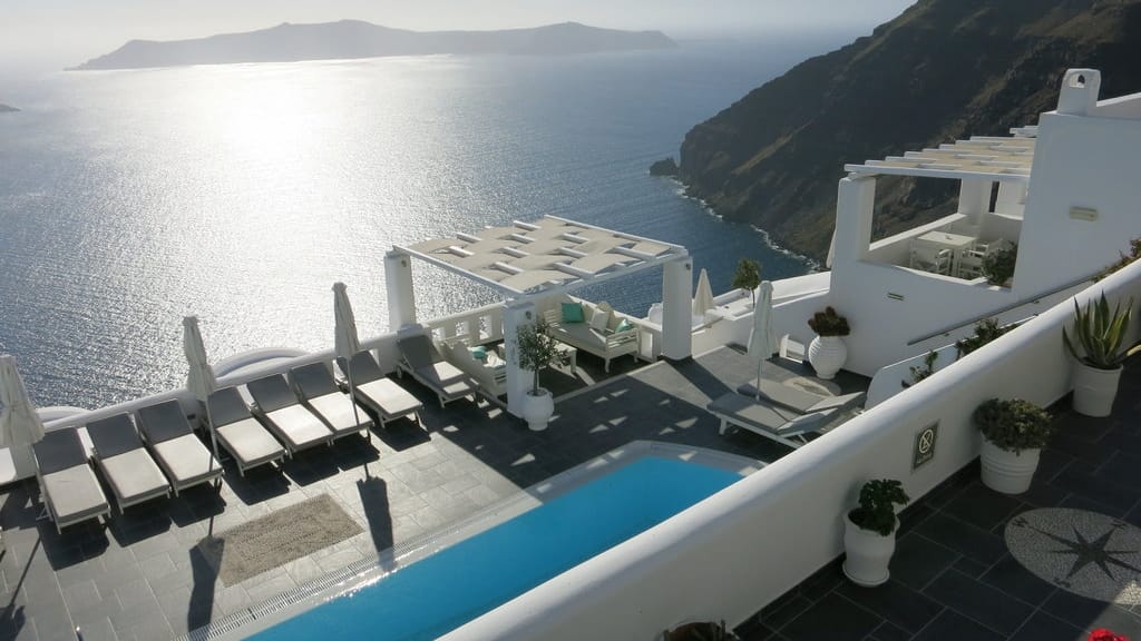 Weiße Häuser und Kirchen mit leuchtend blauen Türen schmiegen sich an die Steilküste der griechischen Insel Santorin. Das 4-Sterne-Hotel Agali Houses bezaubert mit seiner idyllischen Lage.