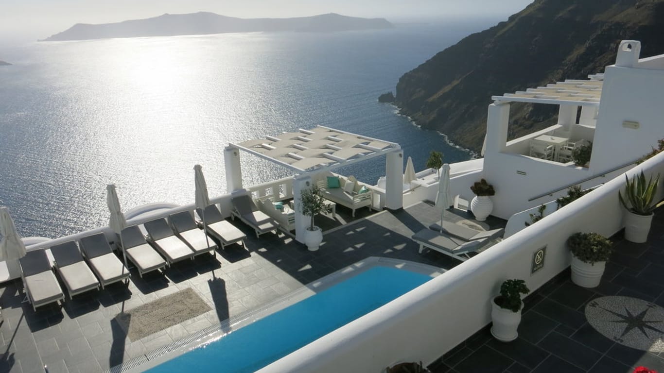 Weiße Häuser und Kirchen mit leuchtend blauen Türen schmiegen sich an die Steilküste der griechischen Insel Santorin. Das 4-Sterne-Hotel Agali Houses bezaubert mit seiner idyllischen Lage.