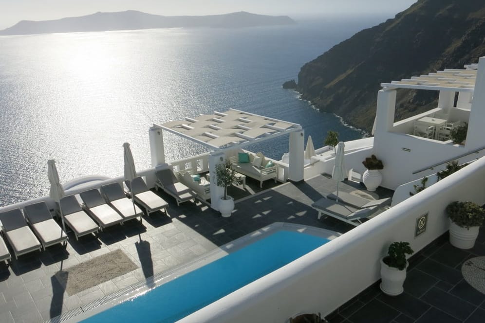 Weiße Häuser und Kirchen mit leuchtend blauen Türen schmiegen sich an die Steilküste der griechischen Insel Santorin. Das 4-Sterne-Hotel Agali Houses bezaubert mit seiner idyllischen Lage.