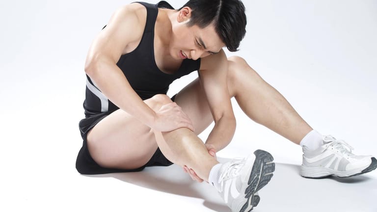 Muskelfaserriss: Ein Mann sitzt auf dem Boden und hält sich die schmerzende Wade.