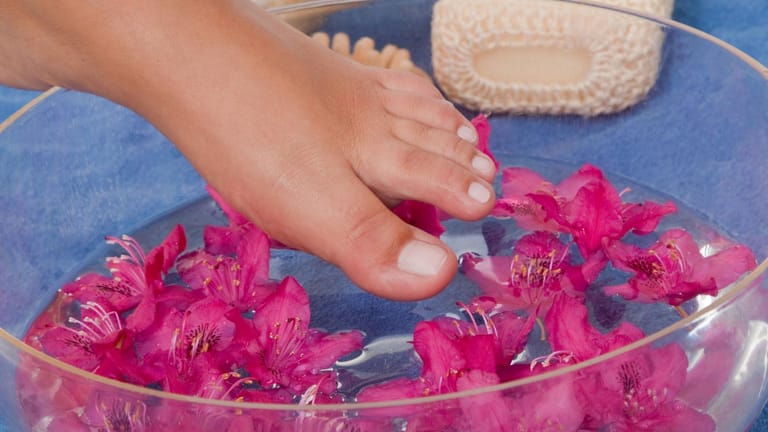 Weiblicher Fuß taucht in Schüssel mit Blütenwasser.