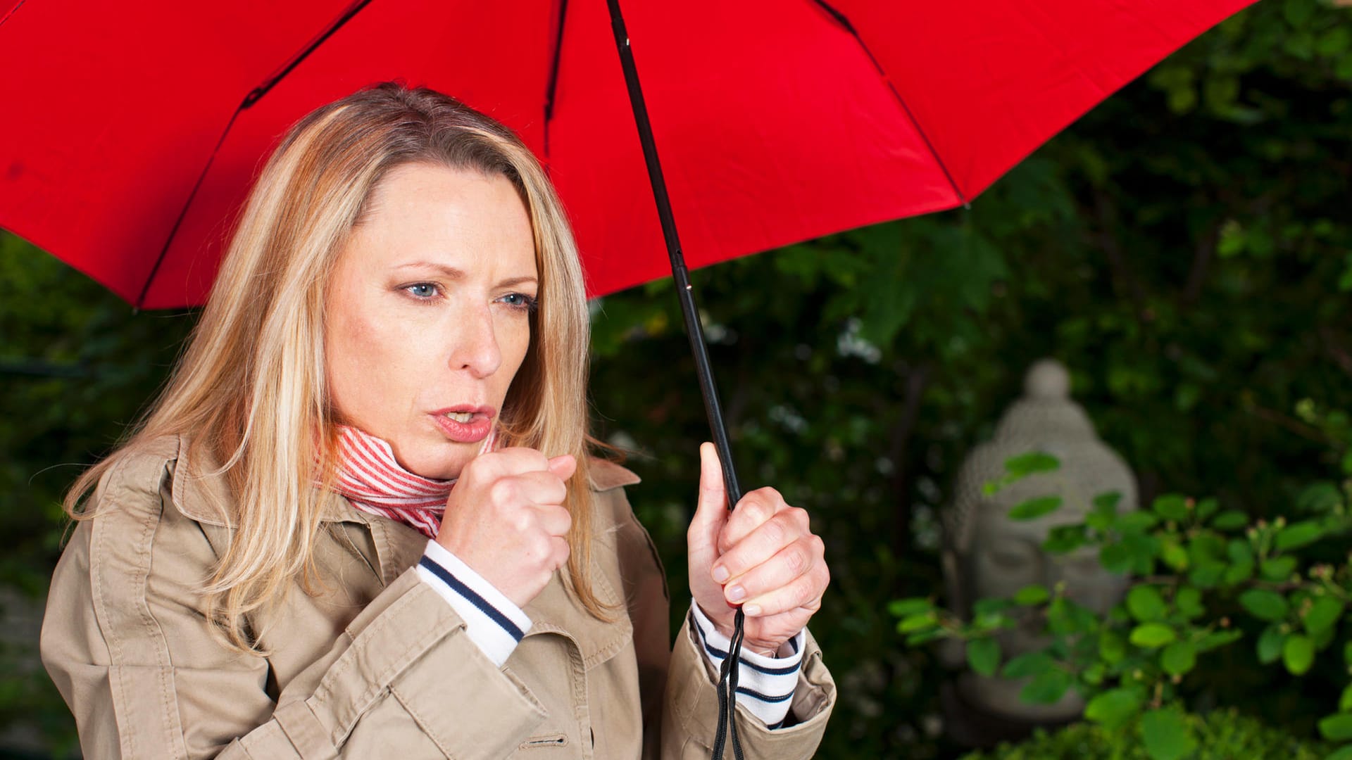 Eine Frau steht unter einem Regenschirm und hustet.