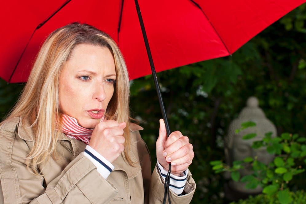 Eine Frau steht unter einem Regenschirm und hustet.