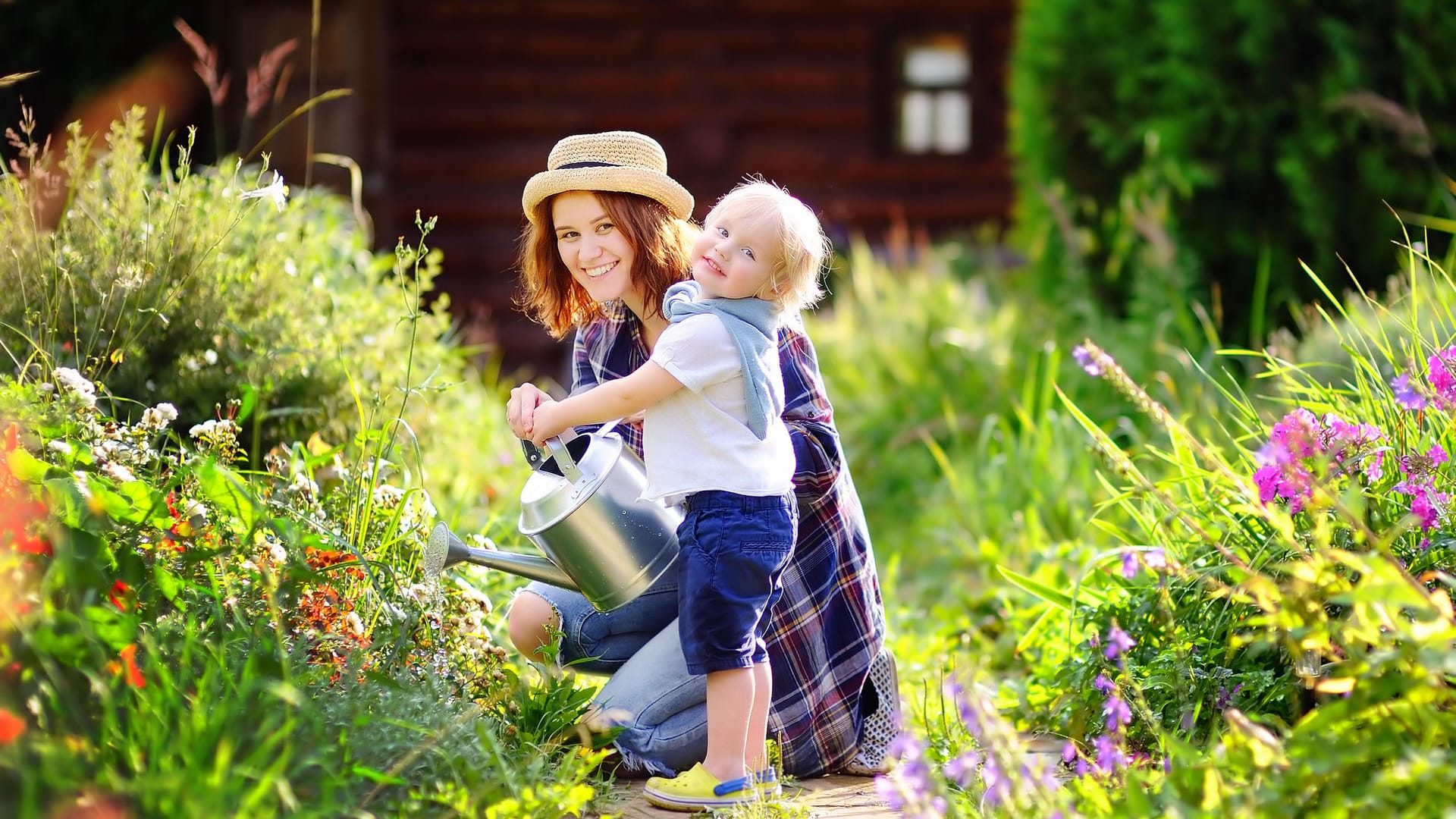 Eine Mutter gießt die Blumen mit ihrem kleinen Kind im Garten