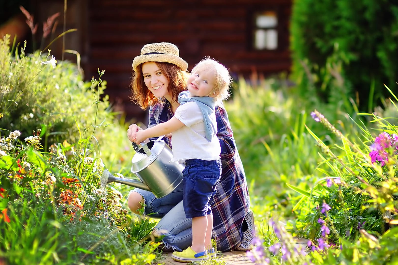 Eine Mutter gießt die Blumen mit ihrem kleinen Kind im Garten