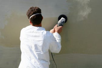 Mann mit Schleifgerät an einer Wand