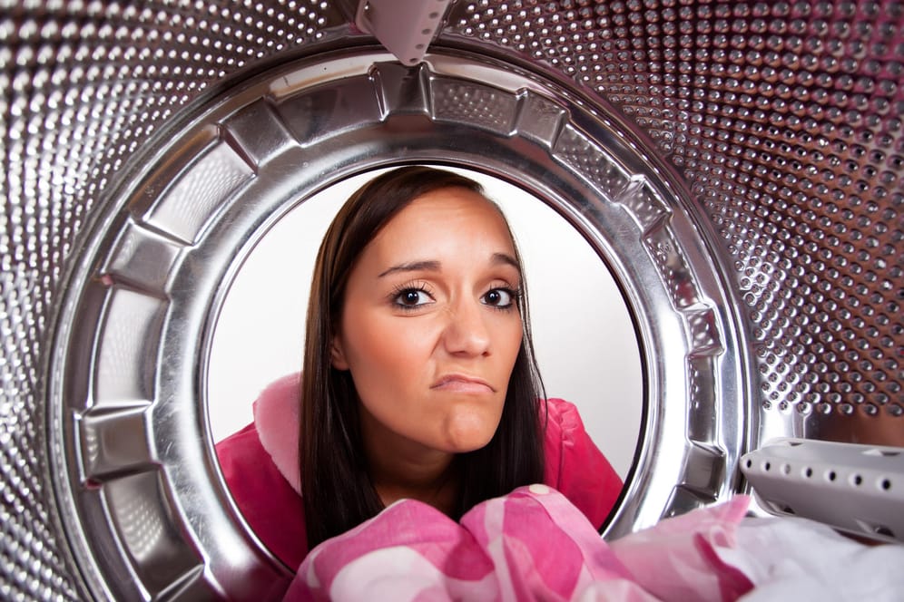 Frau guckt fragend in die Trommel ihrer Waschmaschine