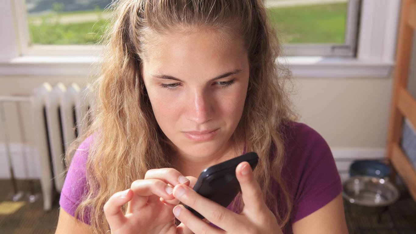 Eine junge Frau mit einer Sehbehinderung tippt auf einem Smartphone.