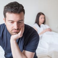 Mann sitzt traurig an der Bettkante von seiner Partnerin abgewendet.