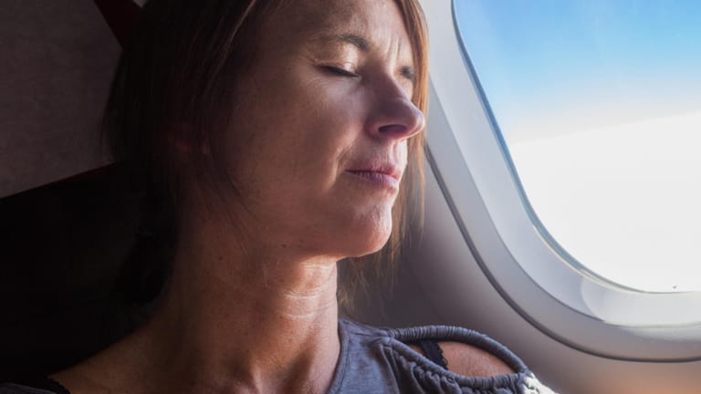 Frau im Flugzeug: Bei Ostflügen sollten Sie möglichst viel schlafen.