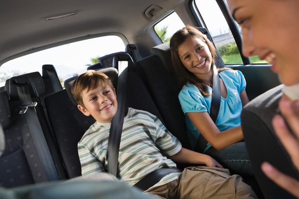 Ein Junge und ein Mädchen sitzen auf der Rückbank: Wenn Sie mit Kindern Auto fahren, sollten Sie für Beschäftigung und Ablenkung für Ihren Nachwuchs sorgen.