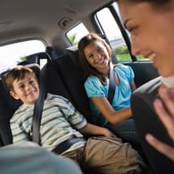 Ein Junge und ein Mädchen sitzen auf der Rückbank: Wenn Sie mit Kindern Auto fahren, sollten Sie für Beschäftigung und Ablenkung für Ihren Nachwuchs sorgen.