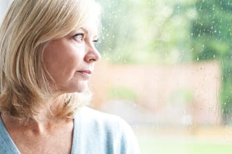 Ältere Frau schaut traurig aus dem Fenster