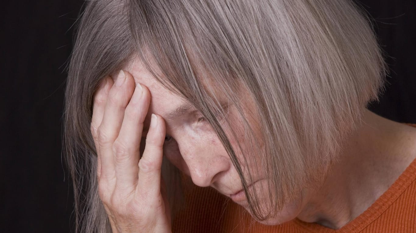 Enzephalitis: Eine ältere Frau fasst sich vor Schmerzen an die Stirn.