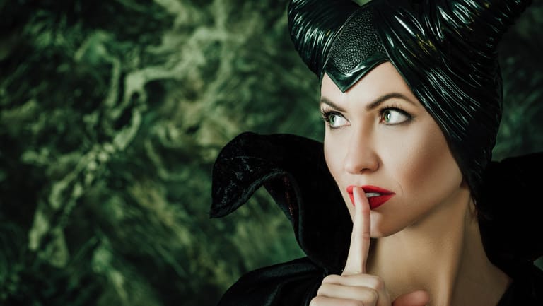 Eine Frau, die als Maleficent verkleidet ist und sich den Finger vor den Mund hält.