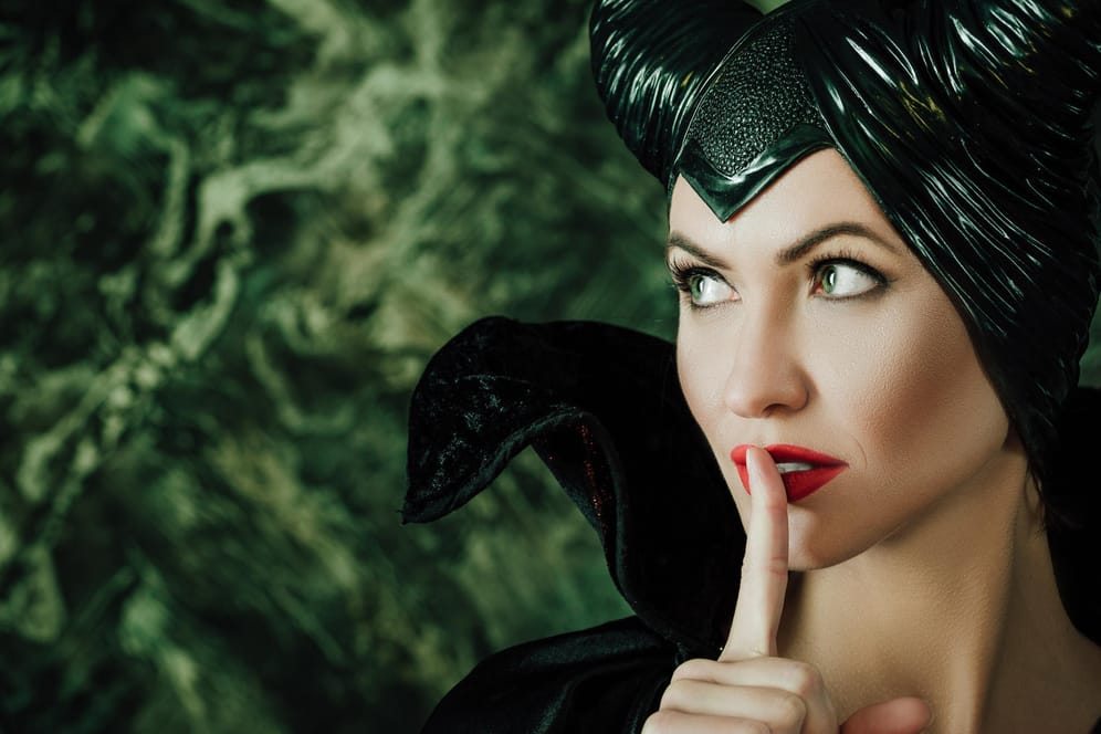 Eine Frau, die als Maleficent verkleidet ist und sich den Finger vor den Mund hält.
