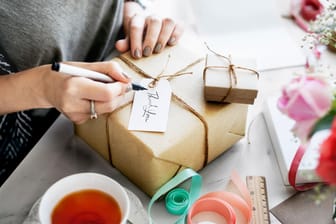Frau schreibt eine Karte an einem Geschenkkarton