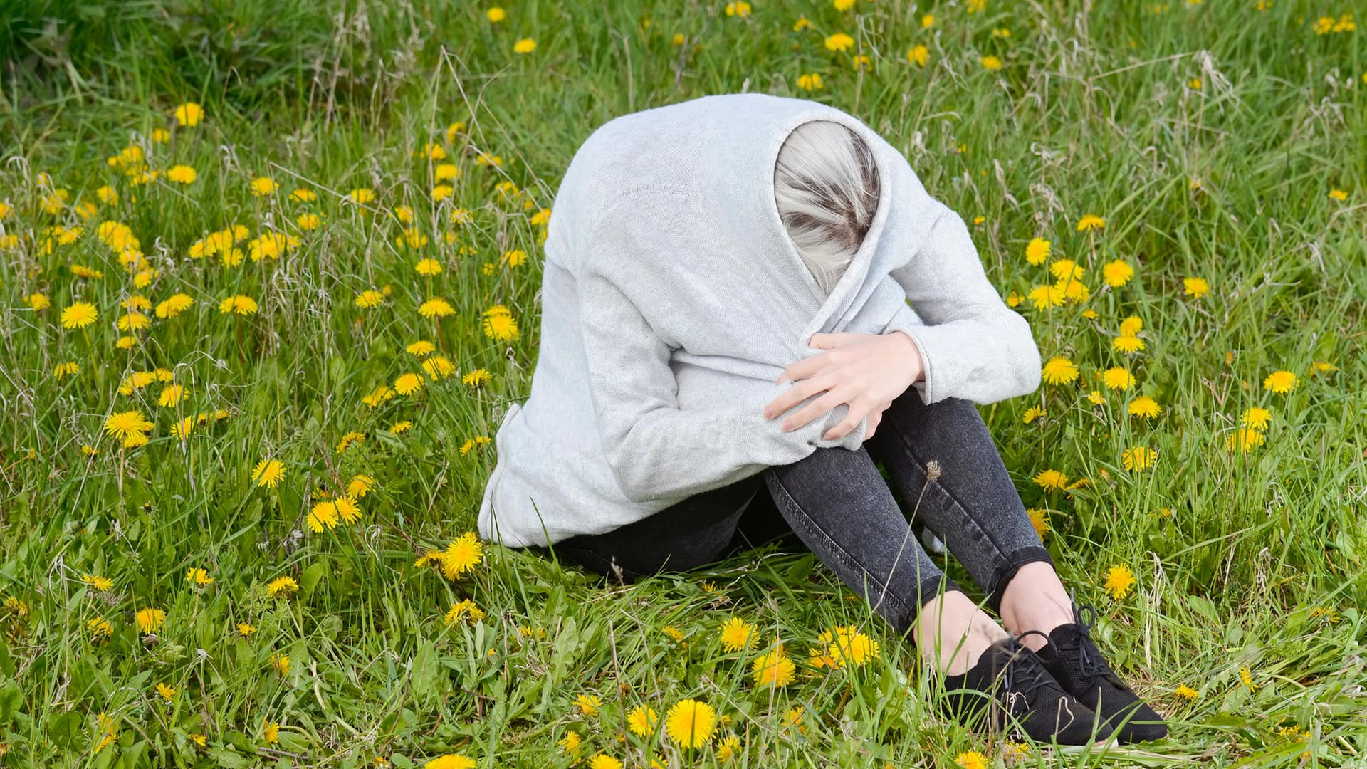 Frau sitzt in Jacke eingewickelt auf einer Wiese