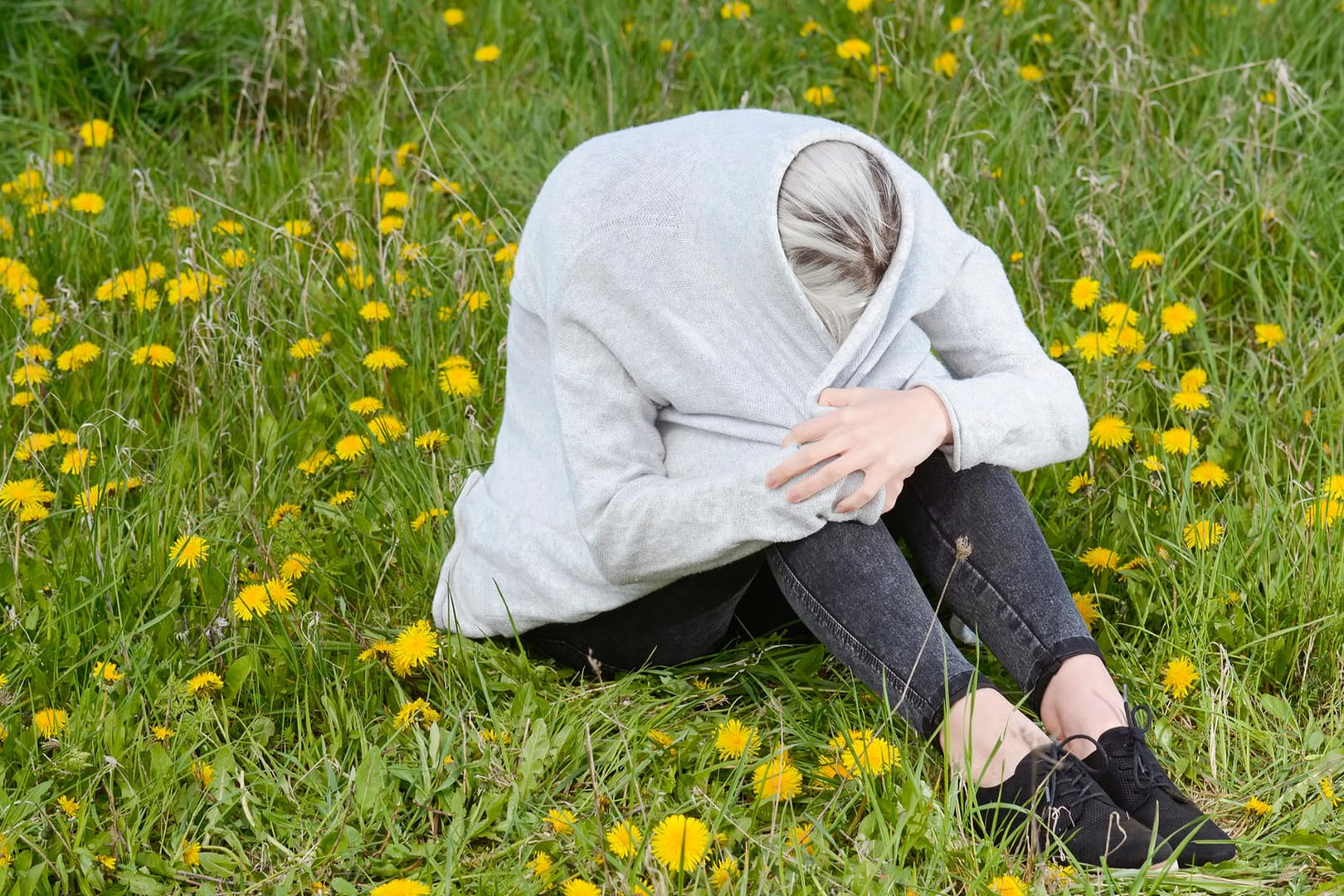 Frau sitzt in Jacke eingewickelt auf einer Wiese