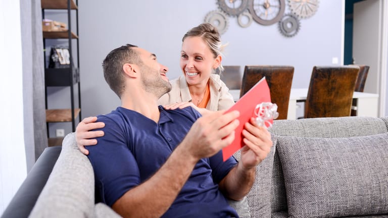 Lächelnde Frau schenkt Mann auf dem Sofa eine Karte