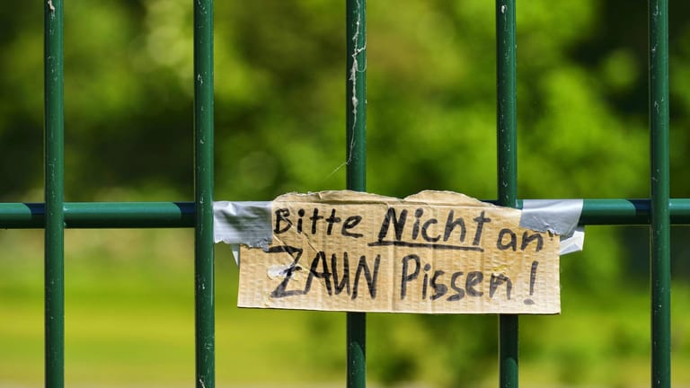 Zaun mit Pappschild: "Bitte nicht an den Zaun pissen!"
