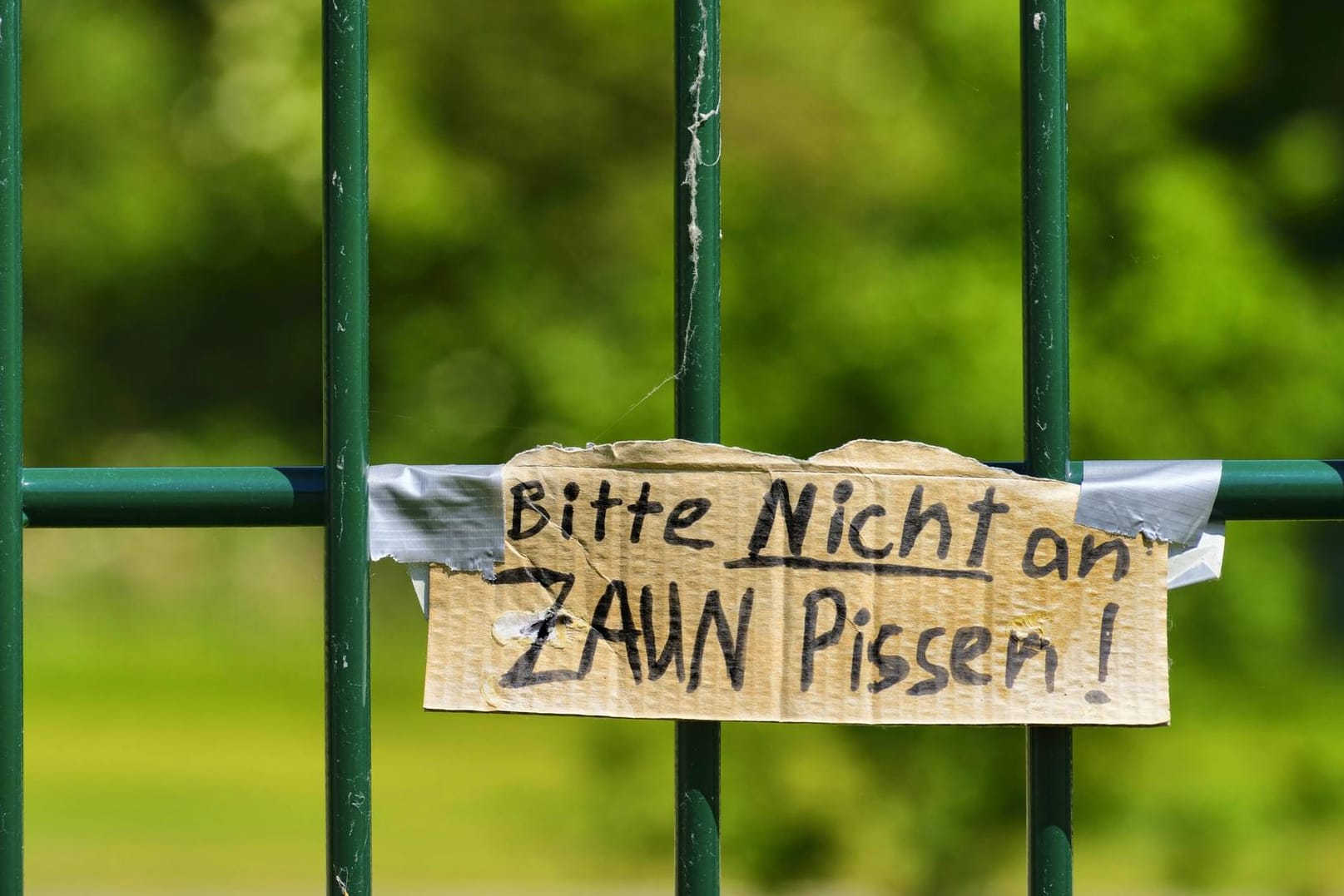 Zaun mit Pappschild: "Bitte nicht an den Zaun pissen!"