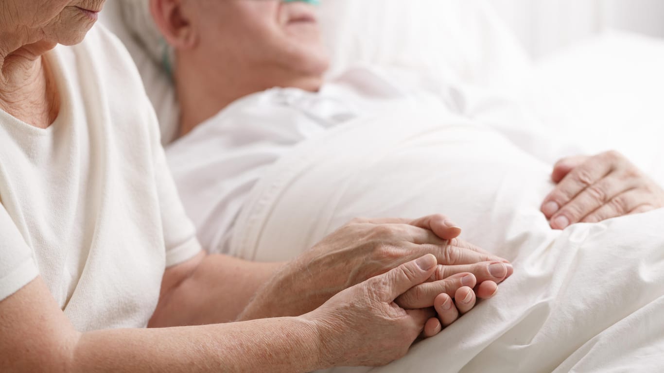 Eine Frau sitzt am Sterbebett ihres Mannes: Manche Menschen berichten von Nahtoderfahrungen. Doch mit welchen Eindrücken gehen wir in den Tod?