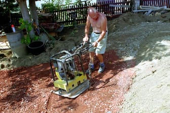 Senior verdichtet den Boden seines Gartens mit einem Bodenverdichter