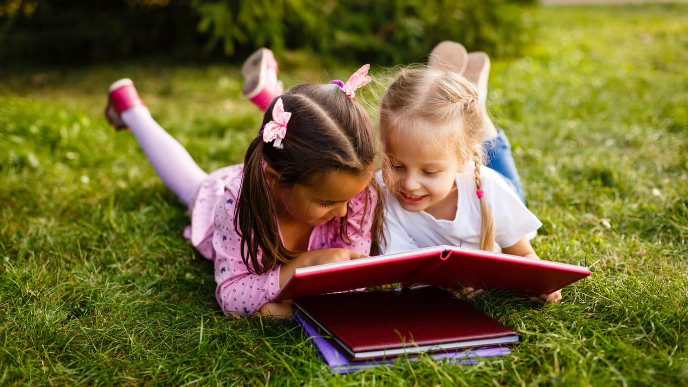 Zwei Mädchen lesen im Gras: Ein Freundebuch ist eine tolle Idee, bei der die Erstklässler auch gleich das Lesen und Schreiben lernen.