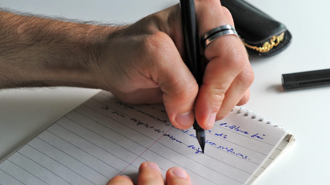 Ein Linkshänder schreibt mit einem Füller auf einen Notizblock.
