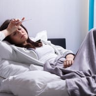 Kranke Frau mit Fieber im Bett: Um das Fieber zu senken, ist Schlaf das beste Mittel.