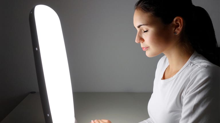 Frau sitzt vor einer Tageslichtlampe: Gegen Winterdepression kann eine Lichttherapie mit speziellen Lampen helfen.