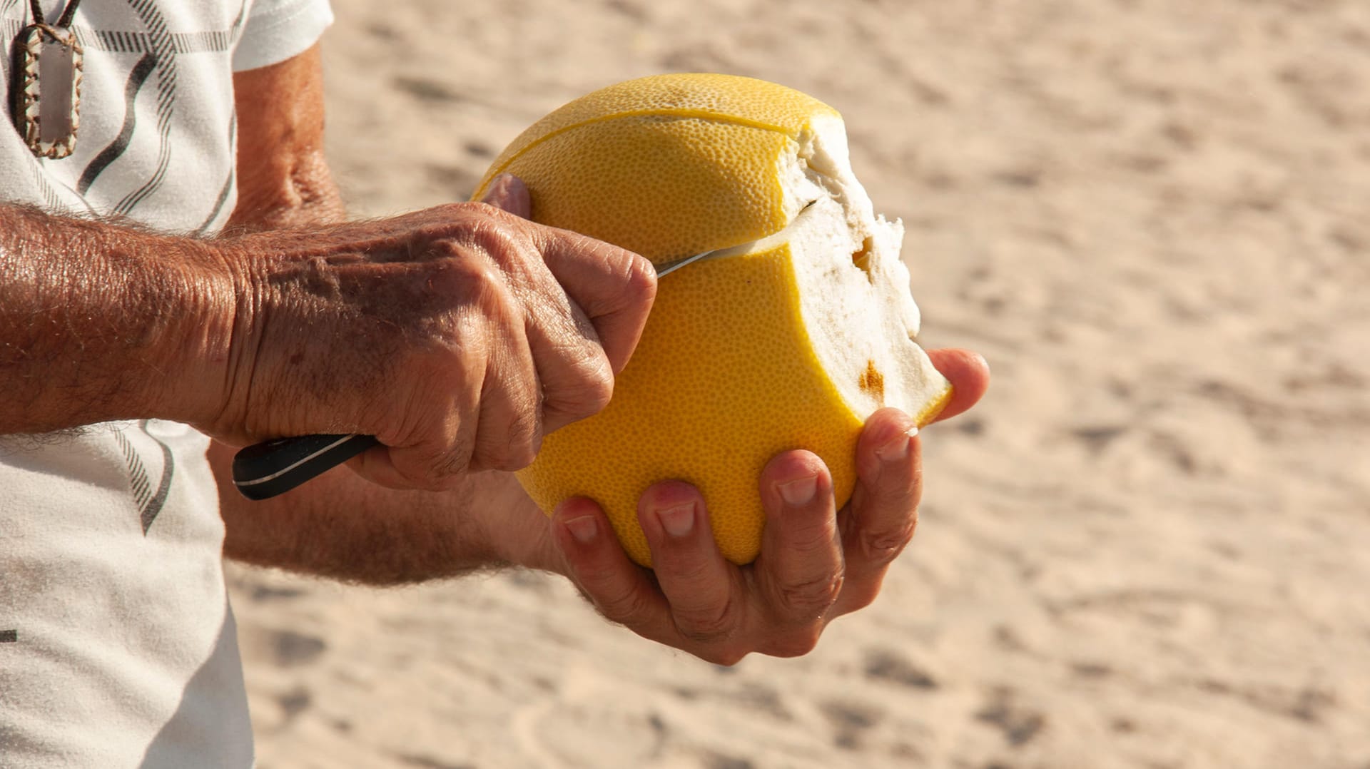 Pomelo wird geschält: Am besten schneiden Sie die Schale ringsum ein paar Zentimeter tief ein.