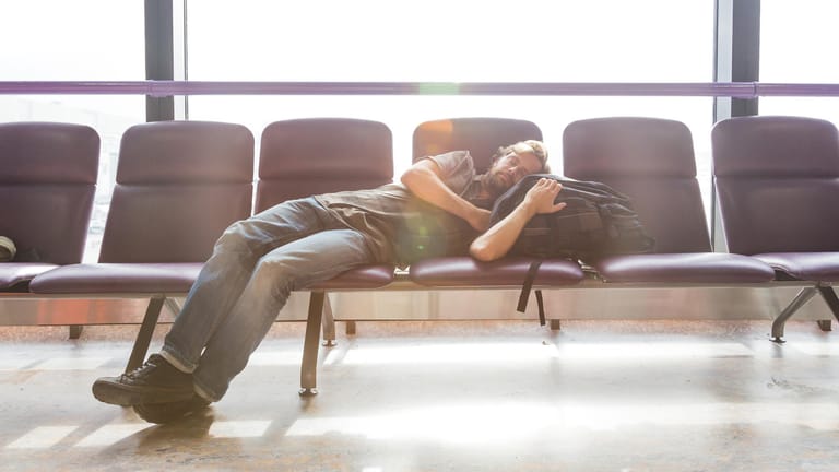 Mann schläft am Flughafen: Eine stressige Reise kann die Entspannung nachhaltig verderben – zum Beispiel wenn Jetlag ins Spiel kommt.